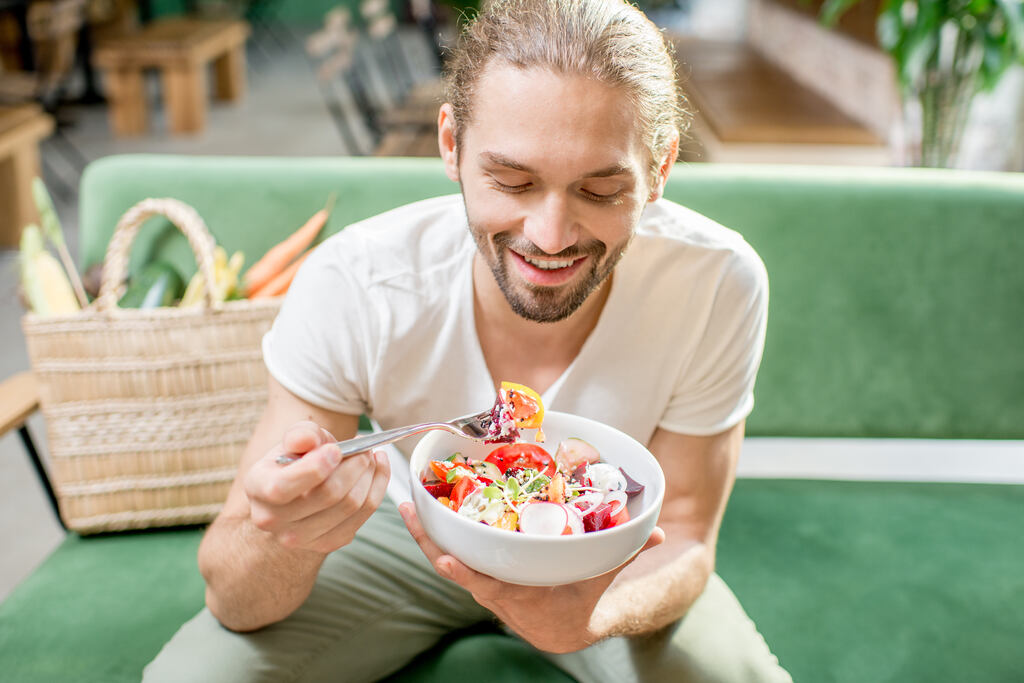 Homem sorridente comendo uma salada, benefícios do óleo de algodão