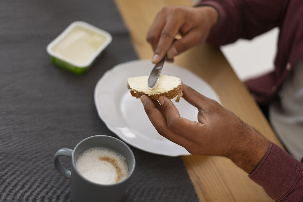 Pessoa passando manteiga no pão durante o café da manhã