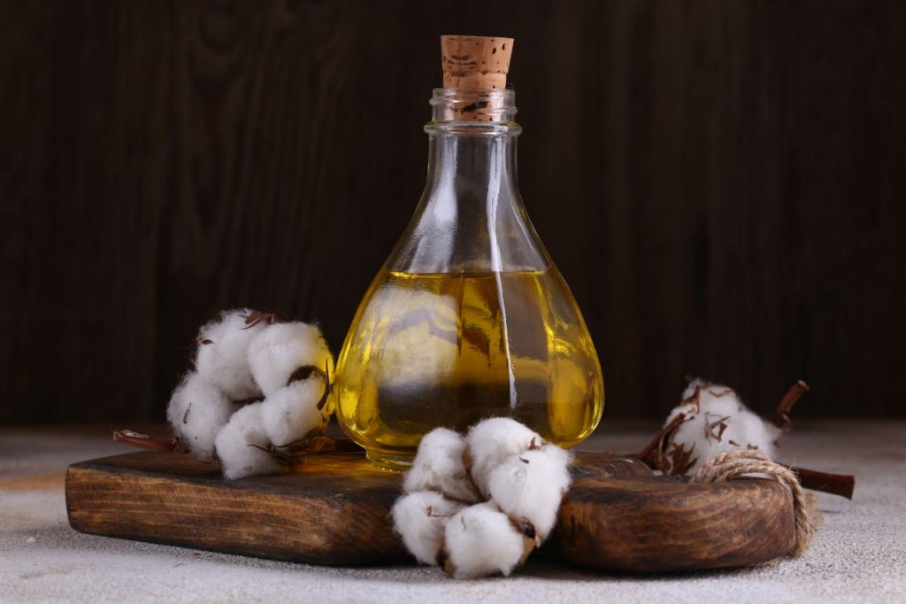 Garrafa de óleo vegetal com rolha sobre tábua de madeira, acompanhada de flores de algodão