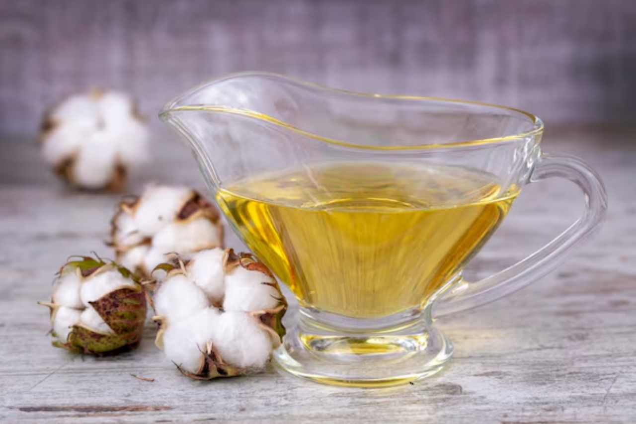 Óleo de algodão em recipiente de vidro ao lado de flores de algodão sobre mesa rústica