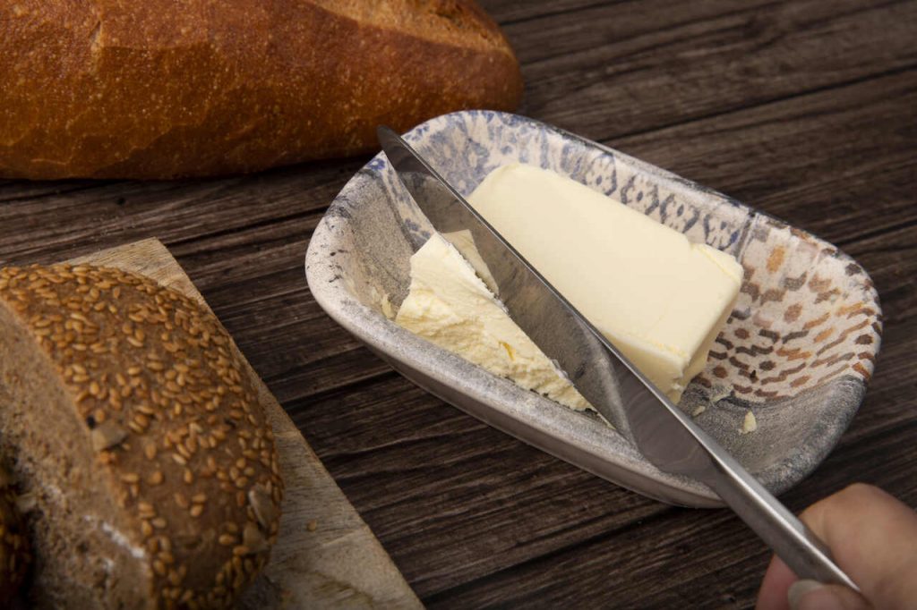 manteiga sendo cortada em prato com pães sobre mesa de madeira