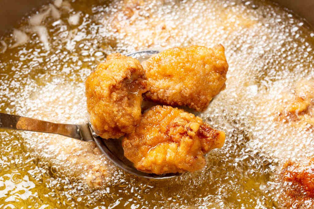 Frango sendo frito em óleo quente, representando uso de gordura vegetal para fritura de alimentos