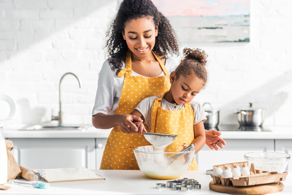 Mãe e filha preparando receita caseira na cozinha com ingredientes para preparo de alimentos