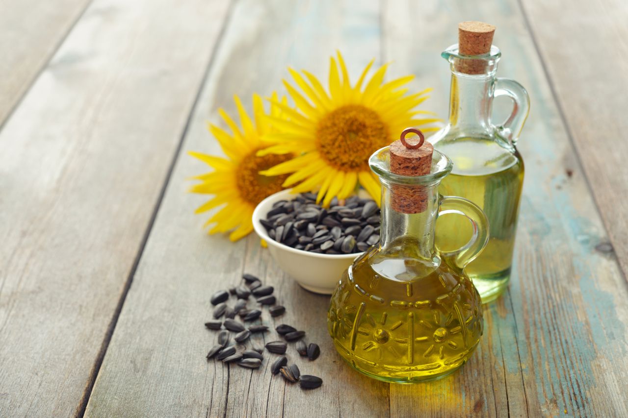 frasco com óleo de algodão ao lado de capulhos de algodão sobre superfície de madeira clara