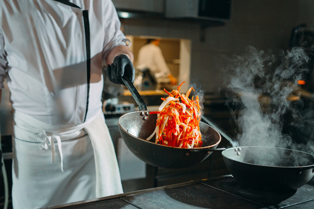 Chef preparando legumes em panela quente, representando escolha do melhor óleo para cozinhar refogados