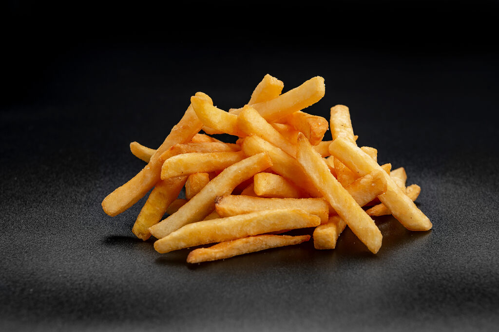 Batata frita dourada e crocante empilhada sobre fundo preto escuro