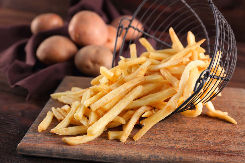 Batatas fritas crocantes espalhadas sobre tábua de madeira com batatas ao fundo