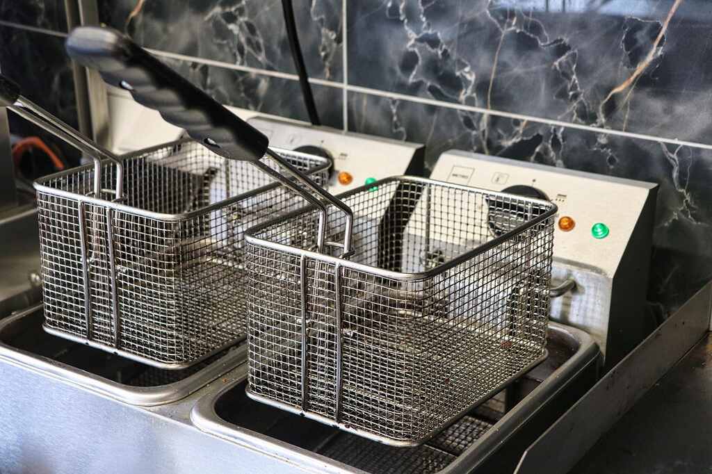 Fritadeira elétrica industrial com cestos metálicos vazios, pronta para uso em cozinha profissional.
