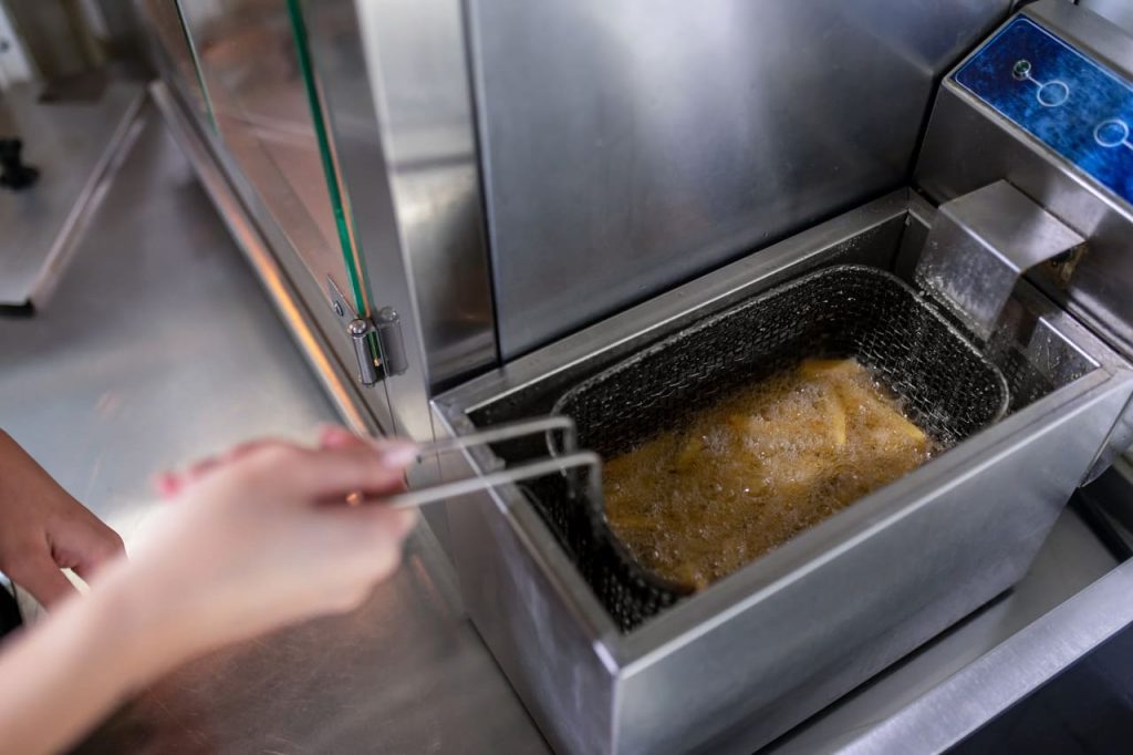 Alimento sendo frito em fritadeira com óleo quente em cozinha profissional