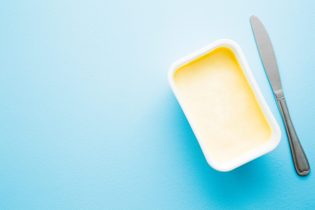 pote de margarina aberto com faca ao lado sobre fundo azul