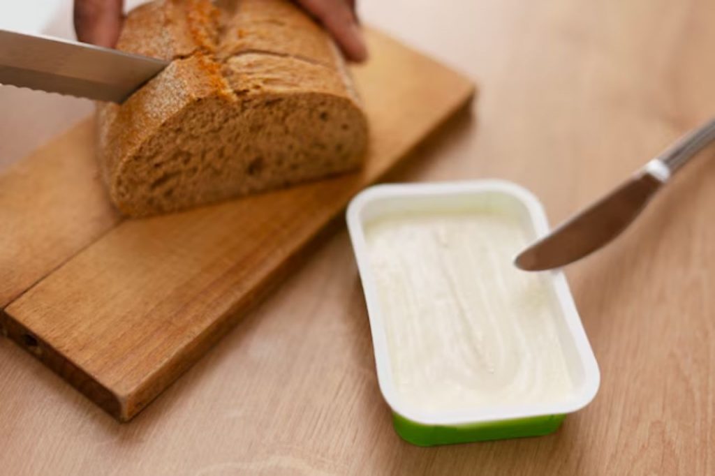 Margarina sendo passada no pão durante preparo de café da manhã simples