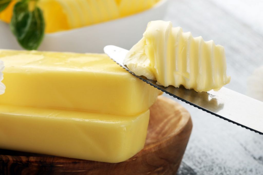 Margarina sendo cortada com faca sobre bloco em superfície de madeira, destacando textura cremosa e consistência