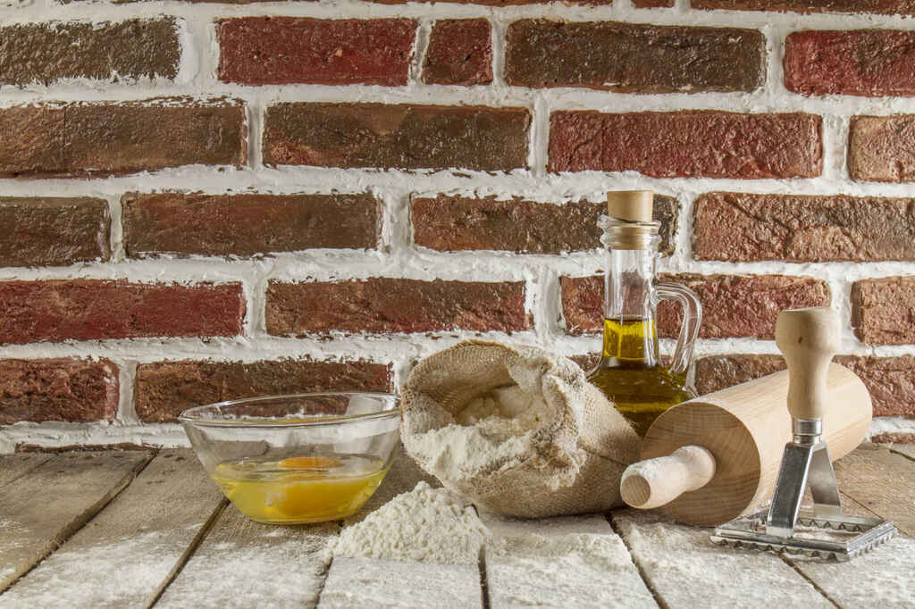Ingredientes culinários com farinha, ovos, azeite e utensílios sobre mesa rústica
