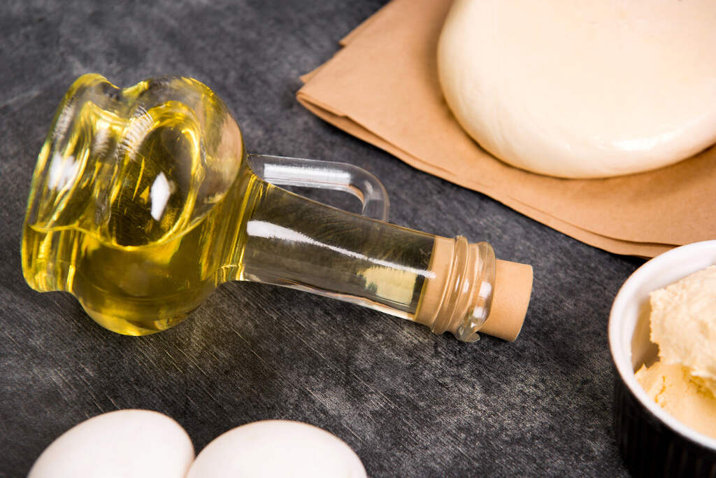 Garrafa de óleo culinário ao lado de massa, ovos e manteiga em preparo de alimentos
