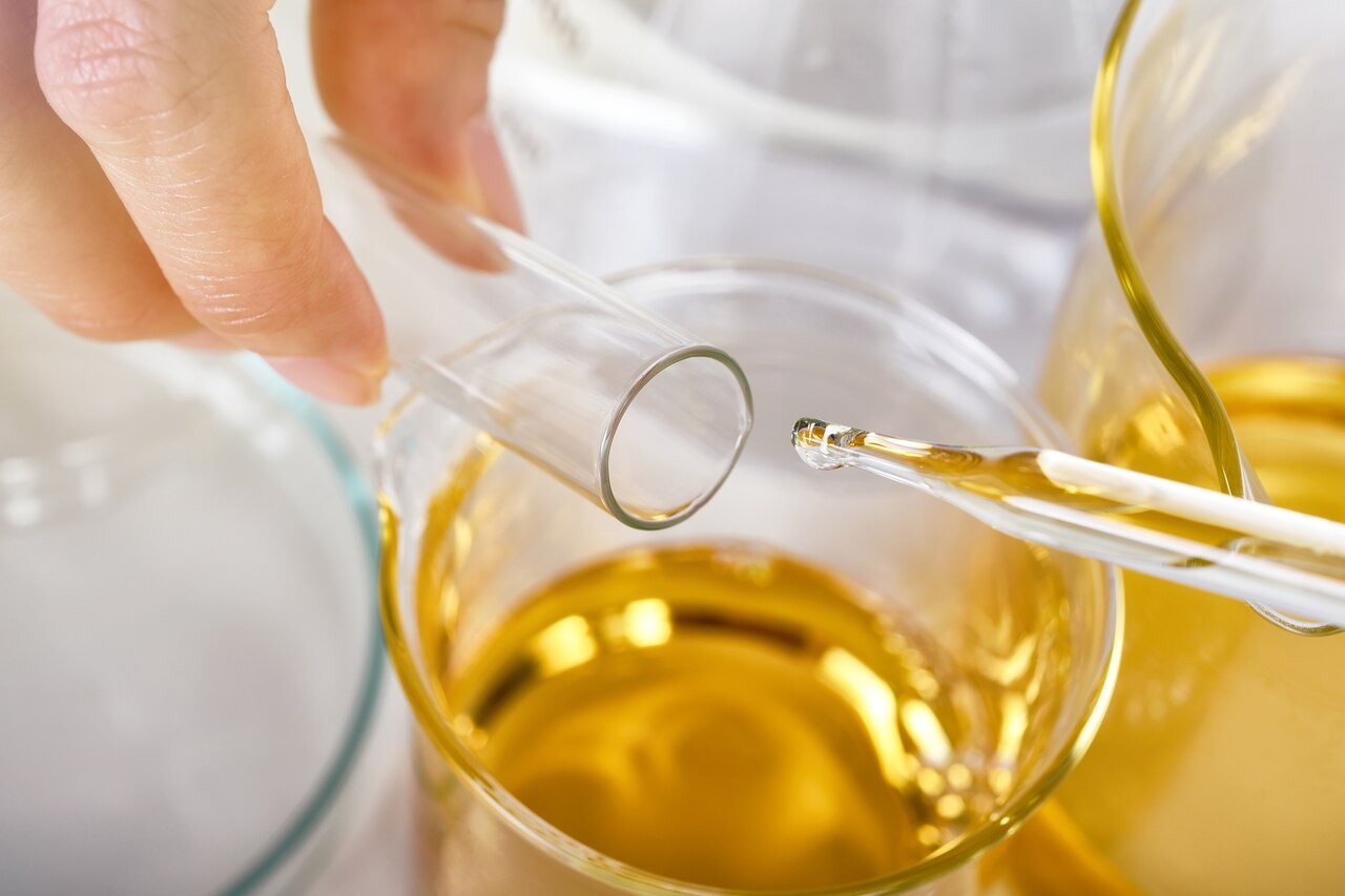 líquido dourado sendo manipulado em recipiente de vidro em laboratório para análise de óleo vegetal