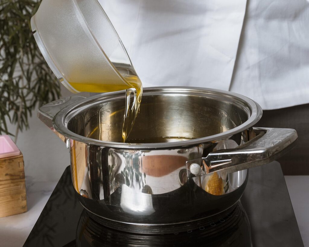 Óleo de cozinha sendo despejado em panela de inox sobre fogão durante preparo de alimentos