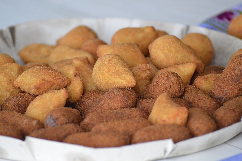 Salgados fritos variados dispostos em bandeja de papel, com coxinhas e bolinhas douradas prontas para consumo.