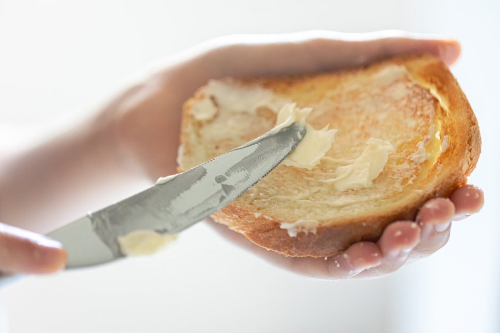 mão passando margarina em pão torrado com faca