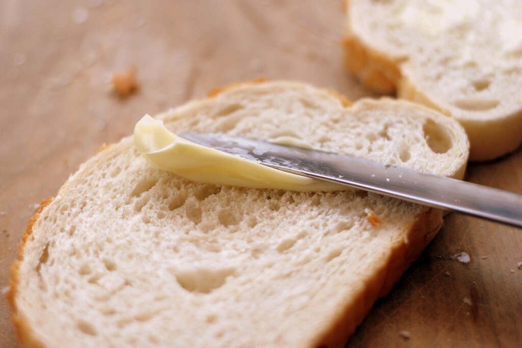 fatia de pão com margarina sendo espalhada com faca