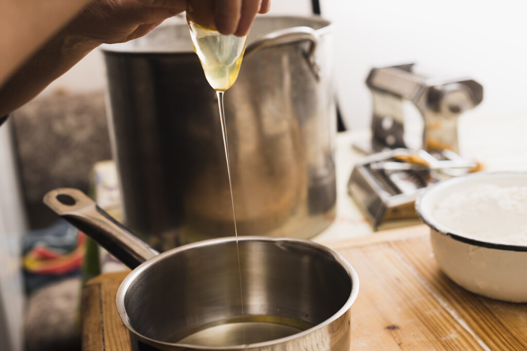 Pessoa adicionando óleo vegetal em panela durante preparo de alimentos em cozinha profissional