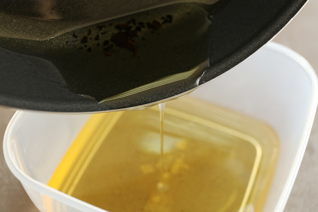 Óleo de cozinha usado sendo transferido de frigideira para recipiente plástico para descarte adequado e reciclagem.