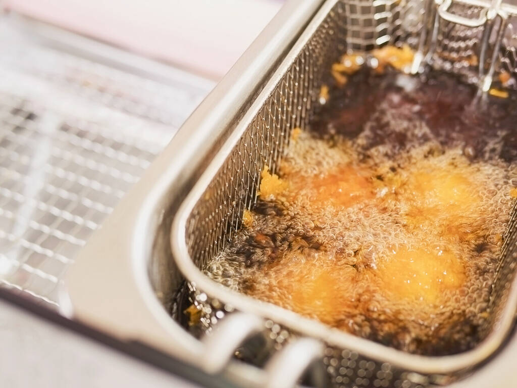 Fritadeira industrial com óleo quente sendo utilizado no preparo de alimentos fritos.