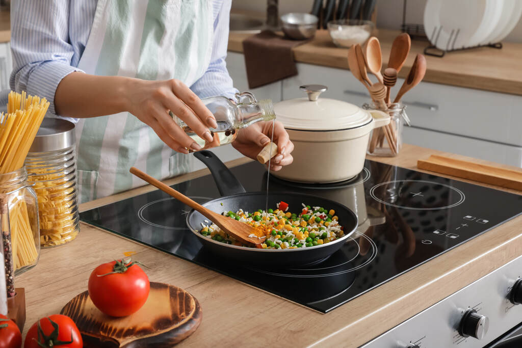 pessoa adicionando óleo em frigideira com legumes sendo preparados no fogão em cozinha doméstica